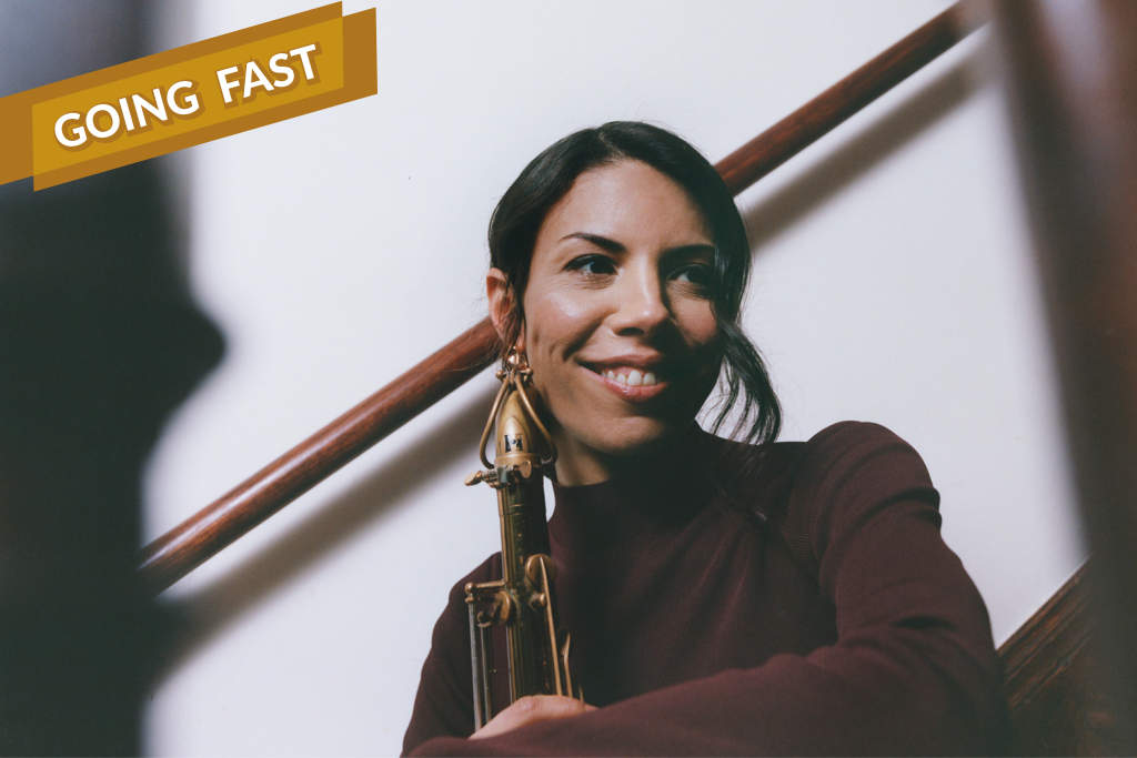 Melissa Aldana leaning on a stair rail holding her saxophone