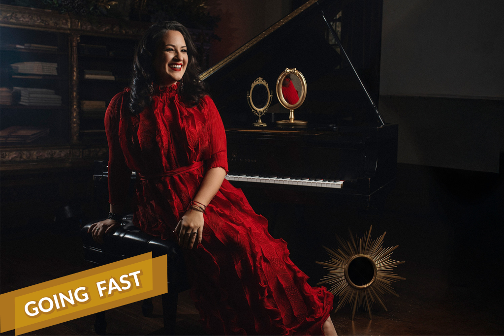 Nicole Zuraitis seated at a grand piano in a red dress, smiling warmly