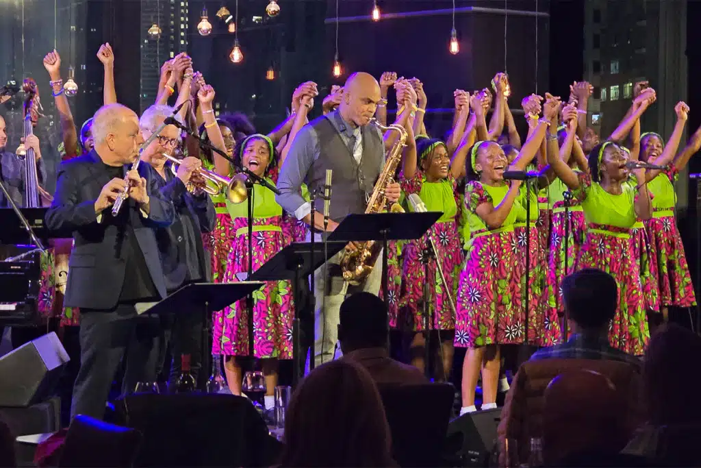 Amina Figarova Sextet and Matsiko World Orphan Choir Liberia on stage, choir in vibrant patterned dresses with sax and brass